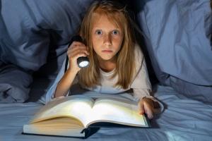 Teen girl reading scary book under covers