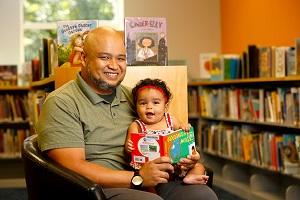 adult holding a child with a book and smiling
