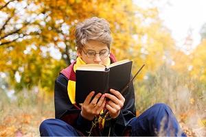 A young person reading a book with a black jacket on that has red and yellow accents