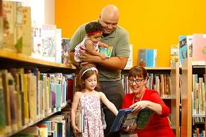 Father and two daughters looking at a book with a librarian