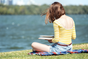 Teen reading a book by a lake