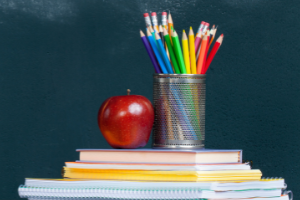 Apple on a stack of books beside a canister of pencils