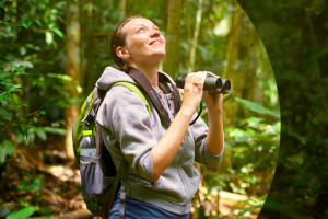someone looking up in the middle of a forest and holding up a pair of binoculars