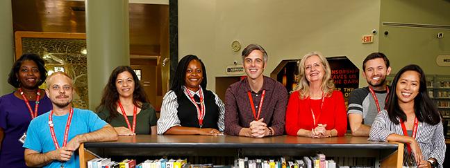 Library workers leaning against a shelf of books