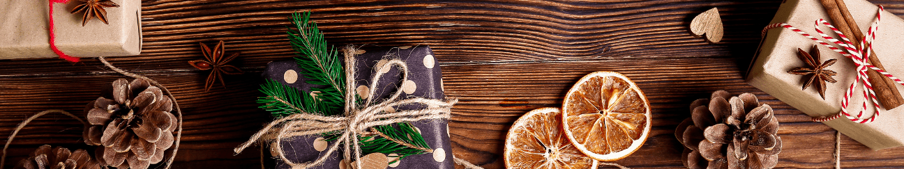 A long thing banner. The background is a wooden surface, with rustic gifts, pinecones, and dried orange slices arrayed around the edges of the image. 