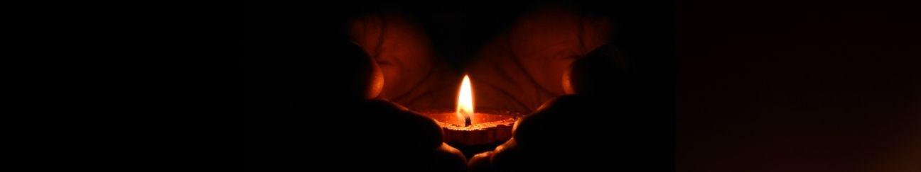 two hands hold a lit candle in darkness