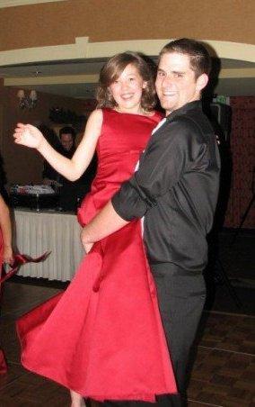 Me in 2007 Photo of a young person in a red dress being lifted up by an older person in all black.