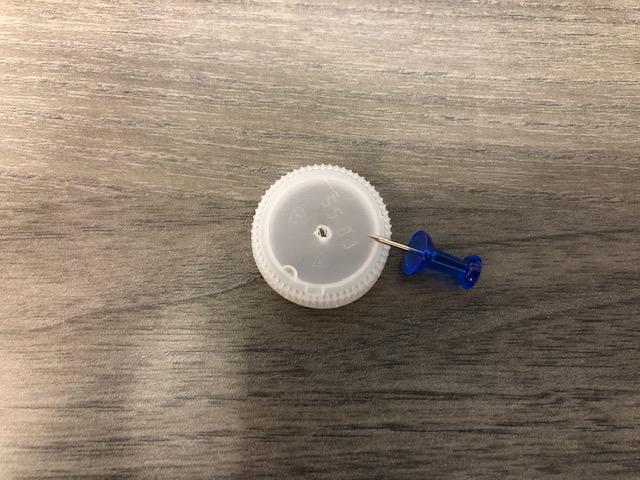 An image of a bottle cap with a hole in the middle next to a pushpin