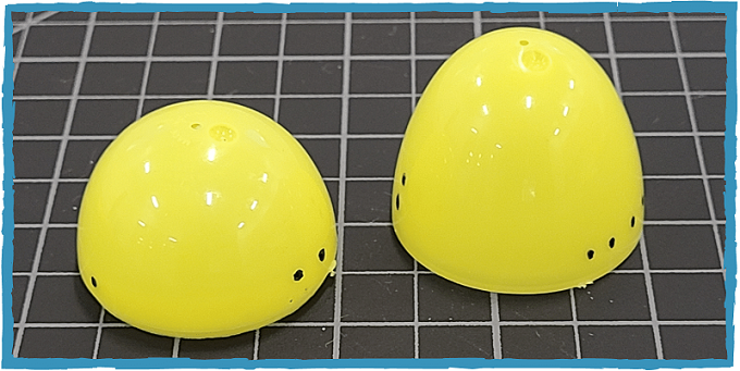 Two halves of a yellow plastic egg sit on a cutting mat. They have a series of dots marked on them in black marker.