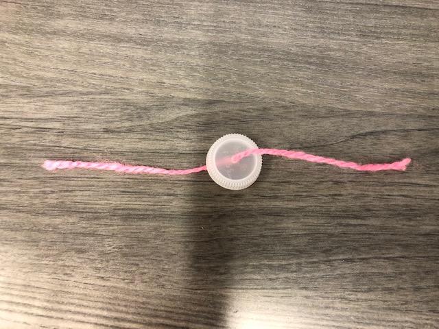 An image of a piece of yarn threaded through a hole in the center of a bottle cap