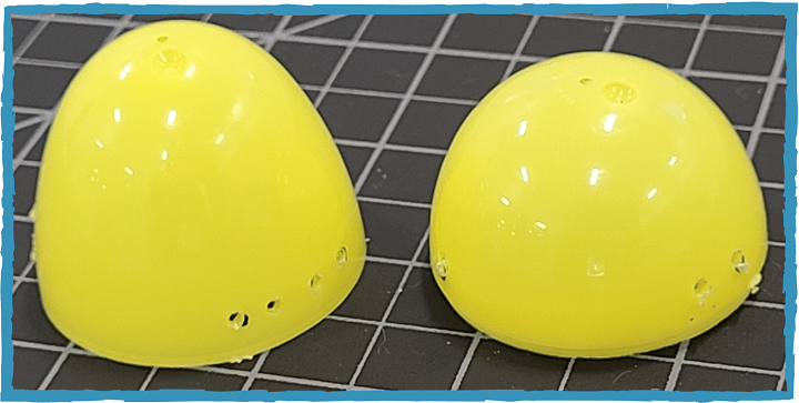 Two halves of a yellow plastic egg sit on a cutting mat. They have a series of holes punched in them.