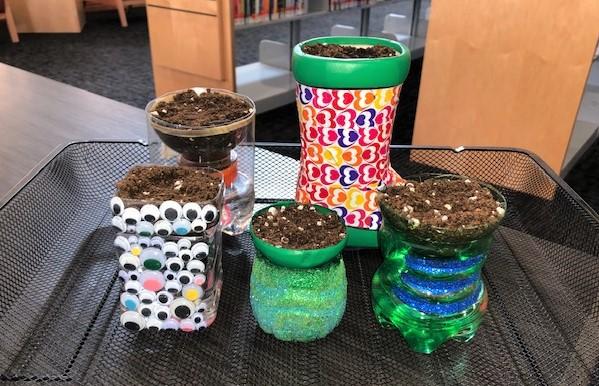 An image of five planters on a tray. Four are made of plastic bottles and one is a ceramic boot