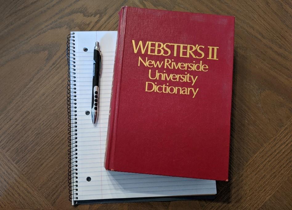 Photo of a red dictionary titled "Webster's II New Riverside University Dictionary" on top of a notebook.