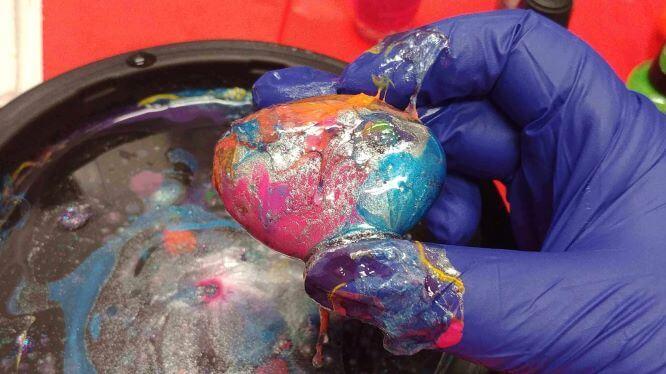 Dipped Rock! A photo of a rock covered in nail polish in a marbled pattern, held between two gloved fingers.