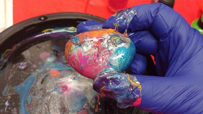 A photo of a rock covered in nail polish in a marbled pattern, held between two gloved fingers.