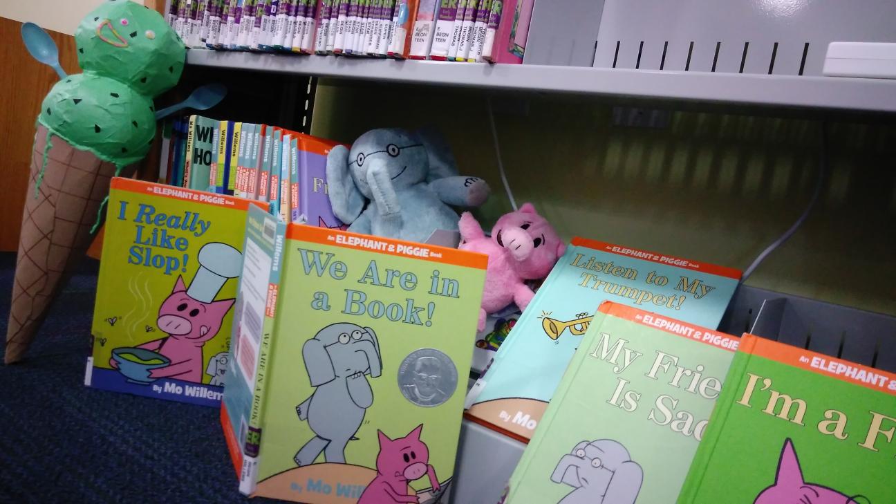 Gerald, Piggie, and Conezilla are surrounded by Mo Willems books
