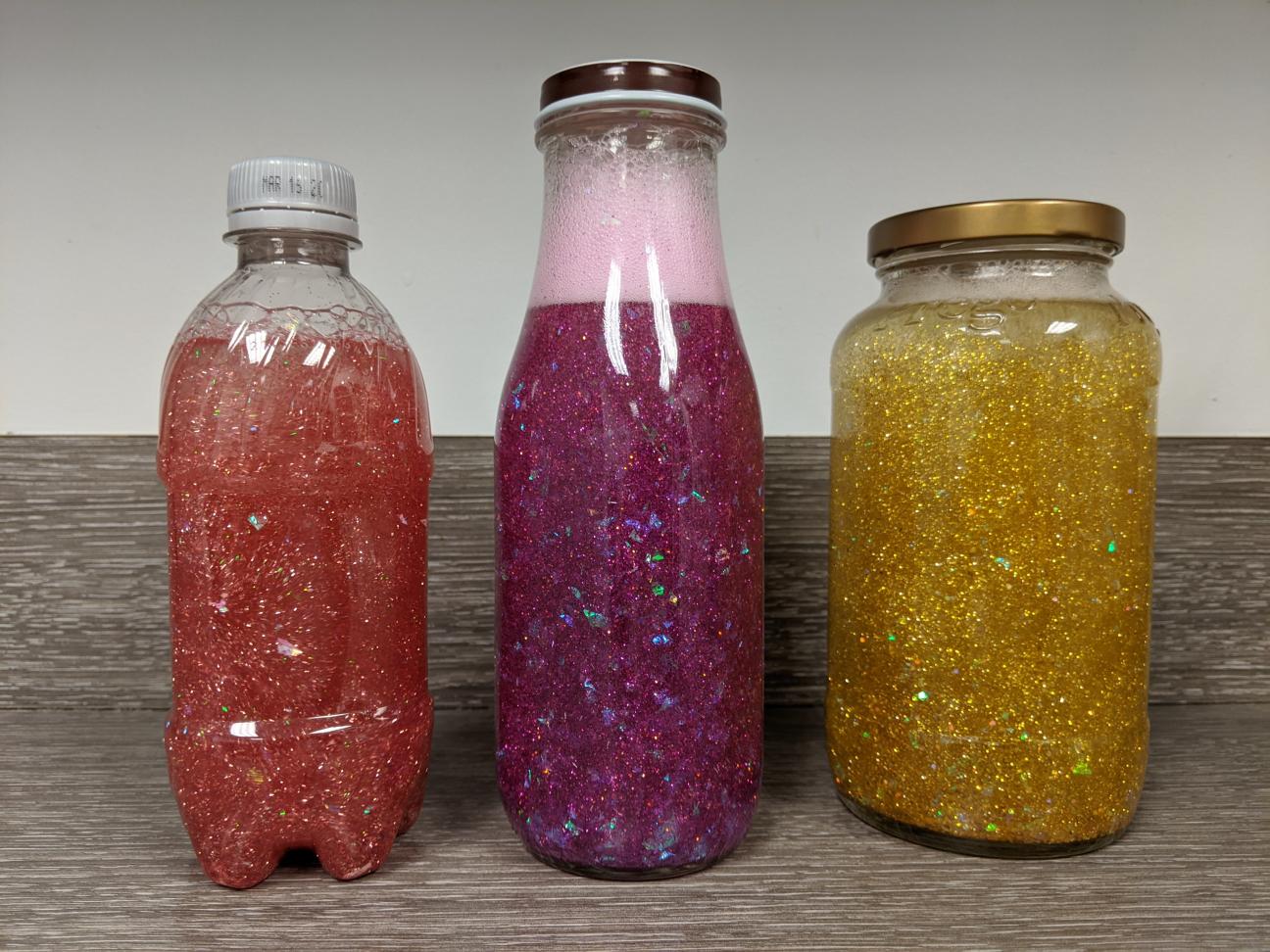 3 calming glitter jars: a small pink one, a larger pink one, and a medium gold one.