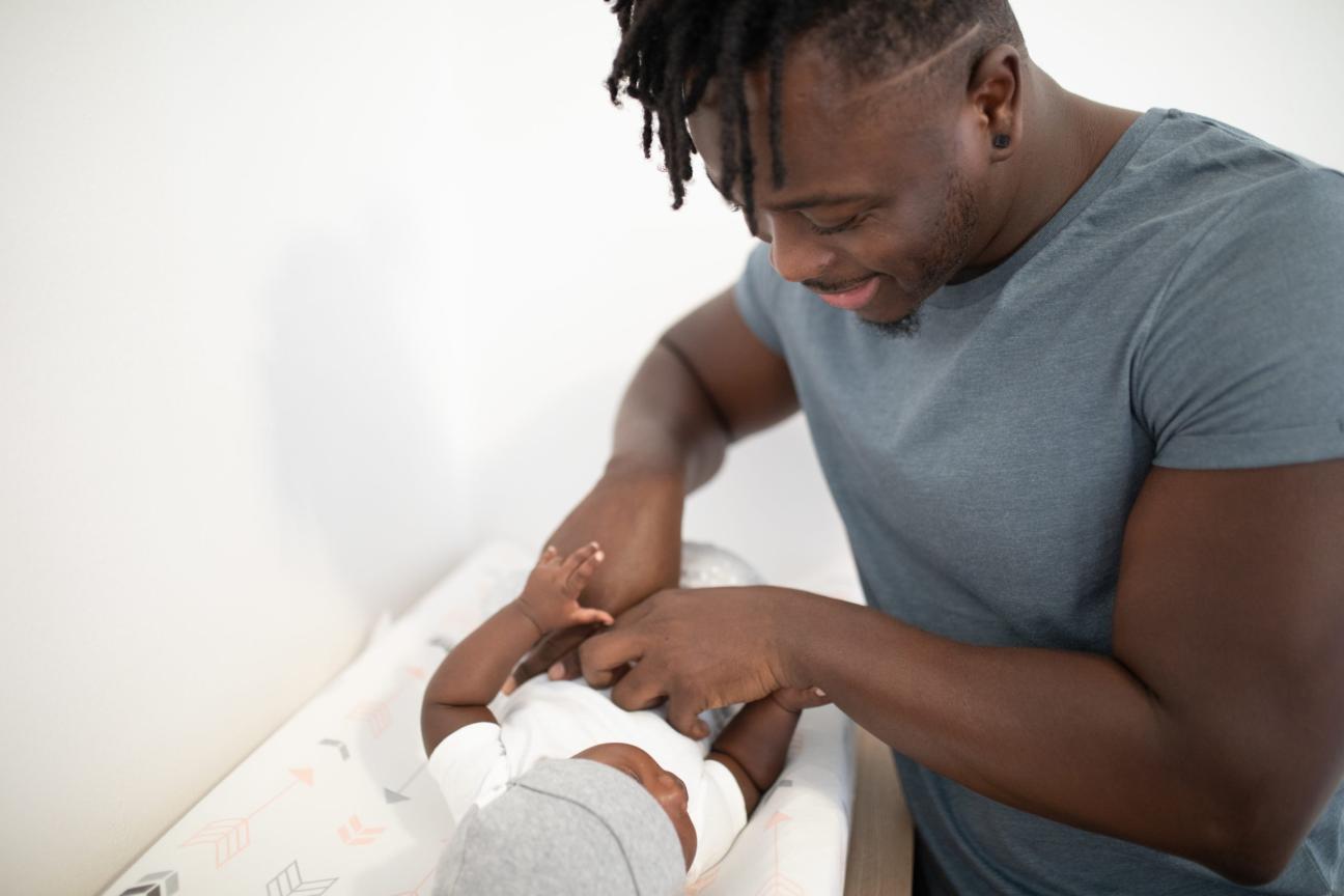 Man touching his baby while lying on white pad Man touching his baby while lying on white pad