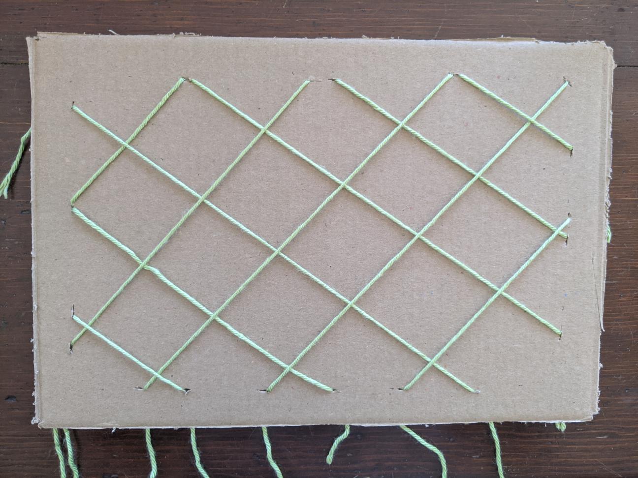The same cardboard with yarn, only now the yarn is secured at each end point along the border.