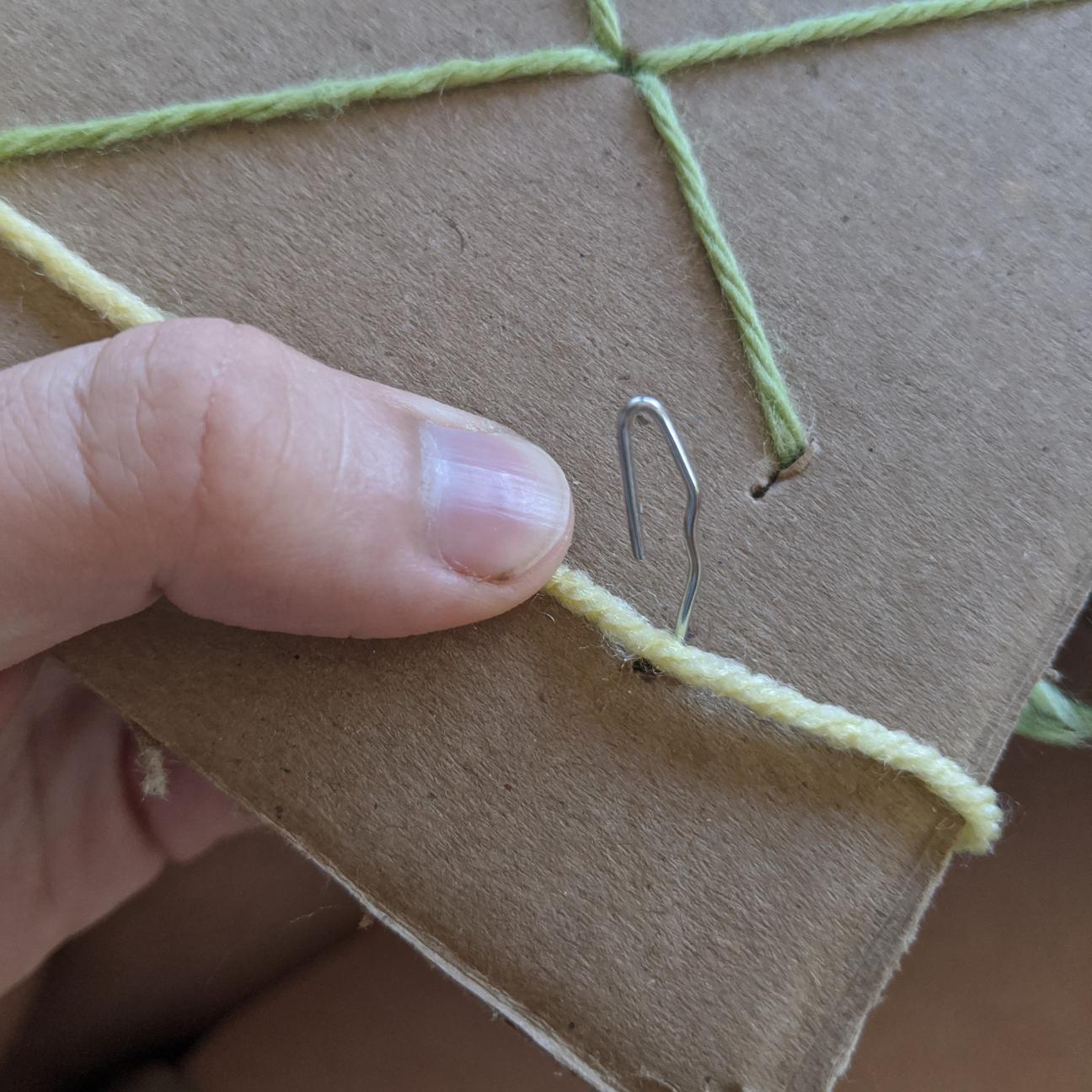 Paperclip hook sticking out of the cardboard, near a strand of yarn.