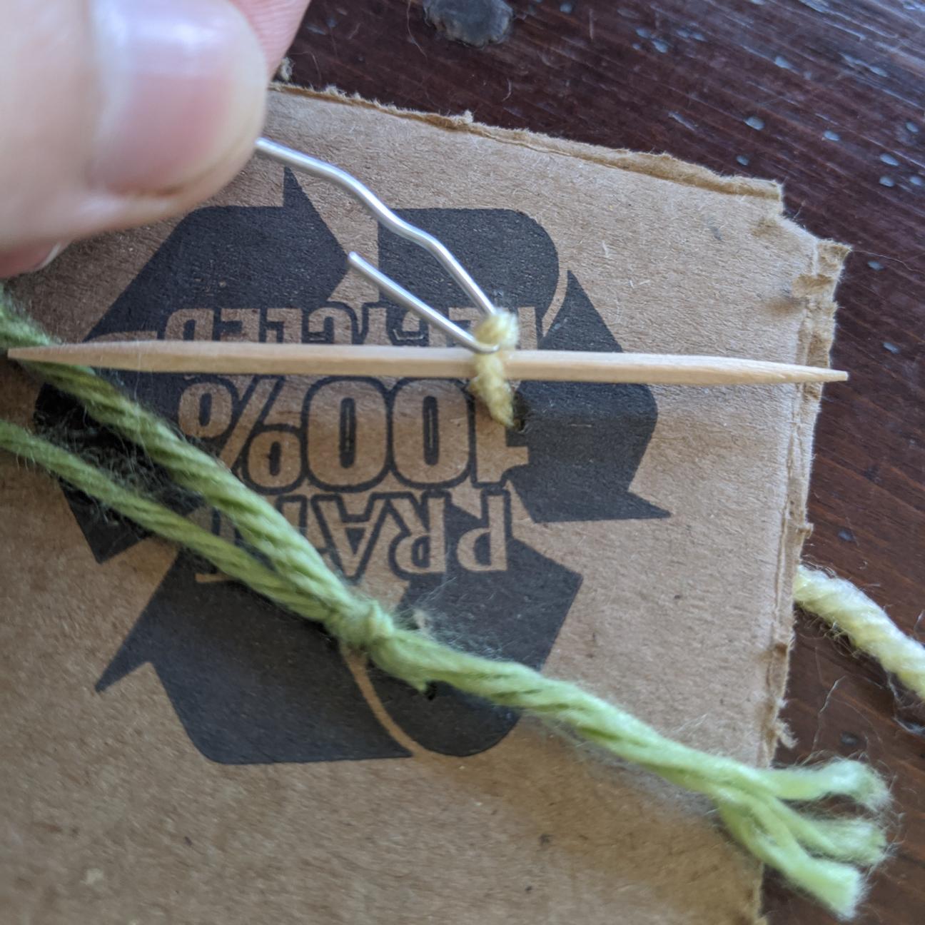 A loop of yarn pulled through cardboard, held with a paperclip hook. There is a toothpick inserted in the loop.