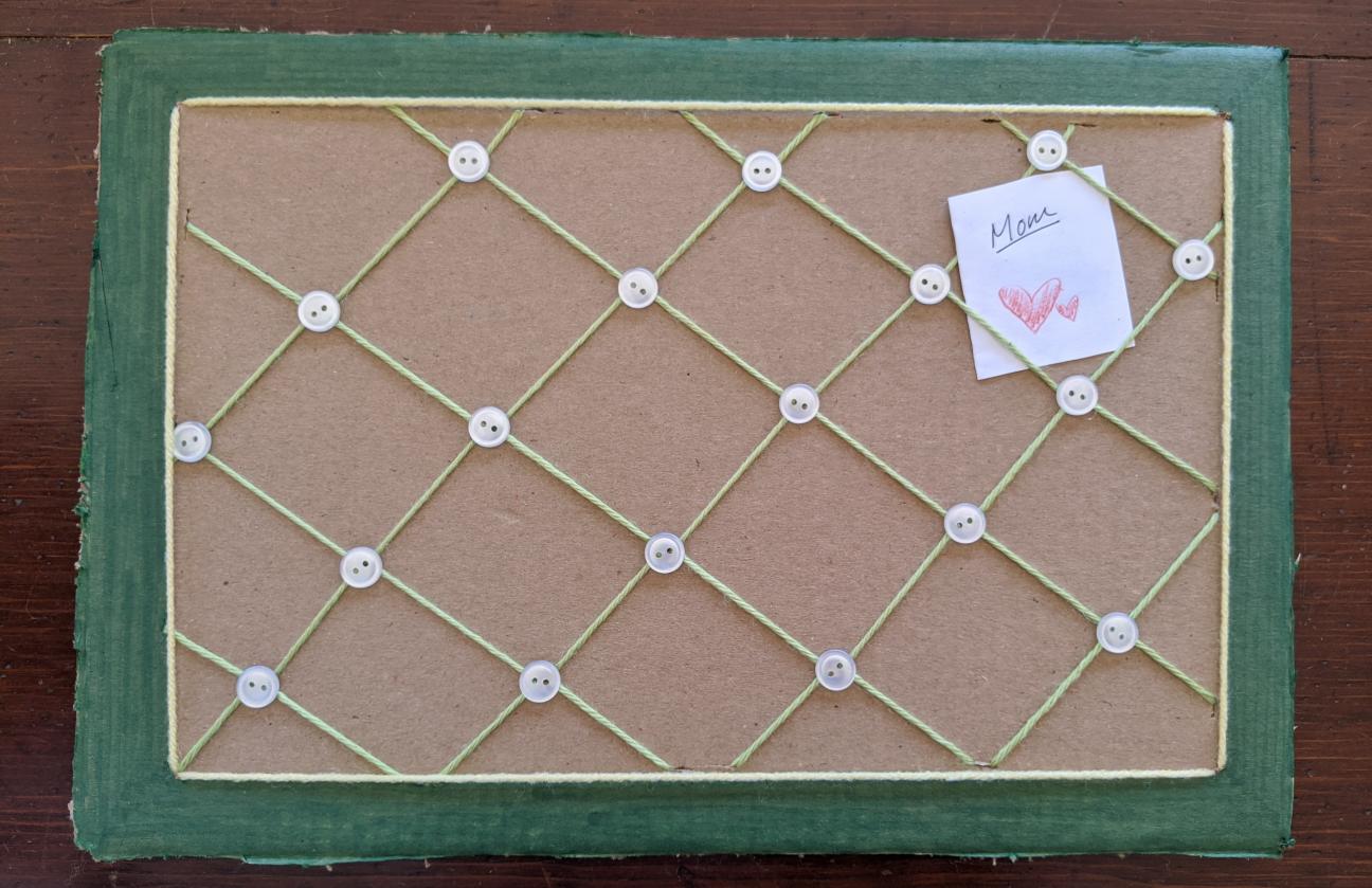 The photo board. The border has now been colored green, and small, shiny white buttons have been glued down at each yarn overlap point.