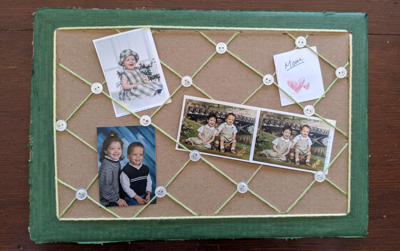 The board from the last photo, with three photos of young children inserted under strands of yarn.