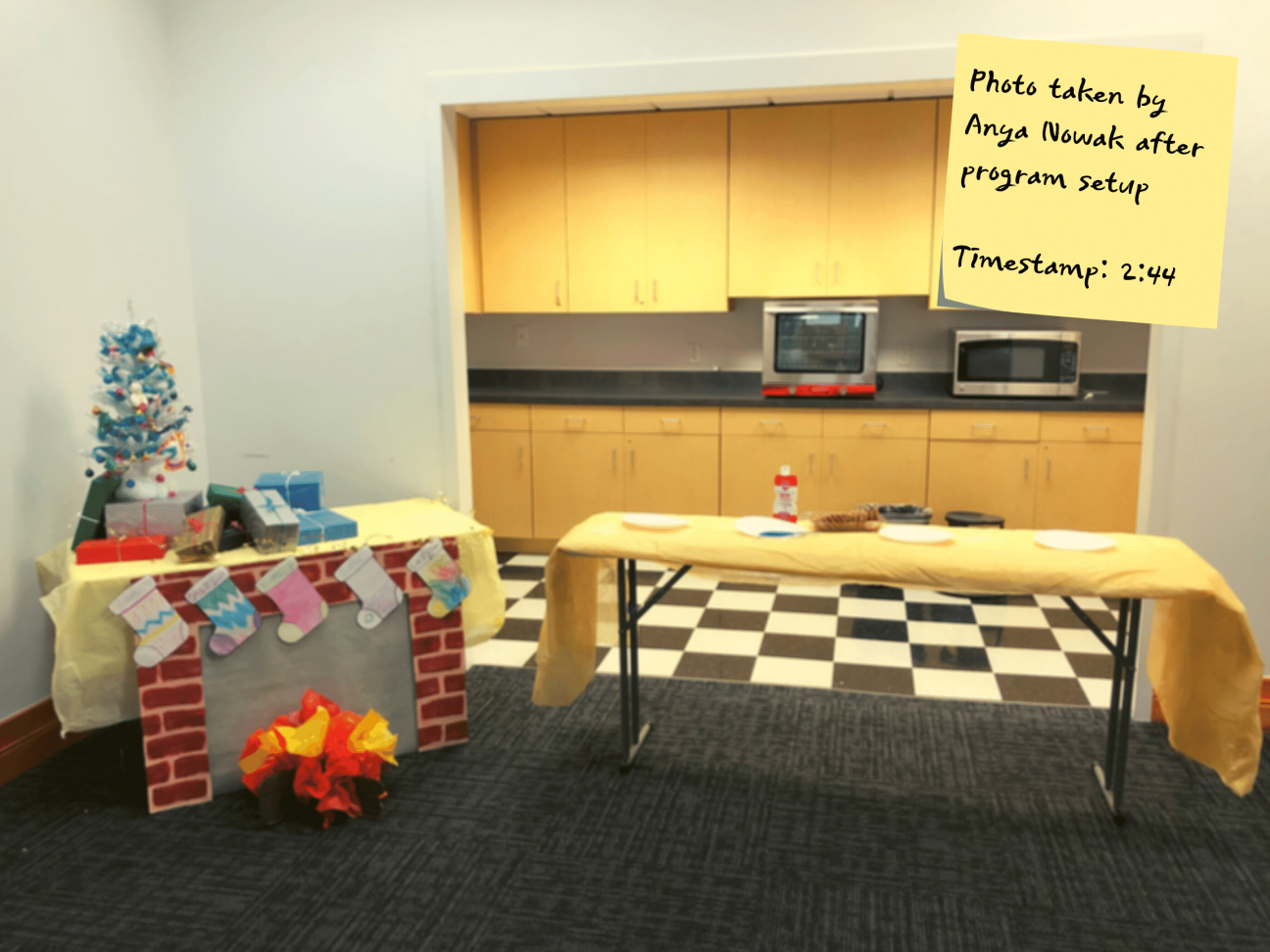Photo taken by Anya Nowak during program setup A photo of a cookie decorating program set up in a public library meeting room. Two tables are side by side. One has holiday decorations and one has empty plates and a container of cookies.