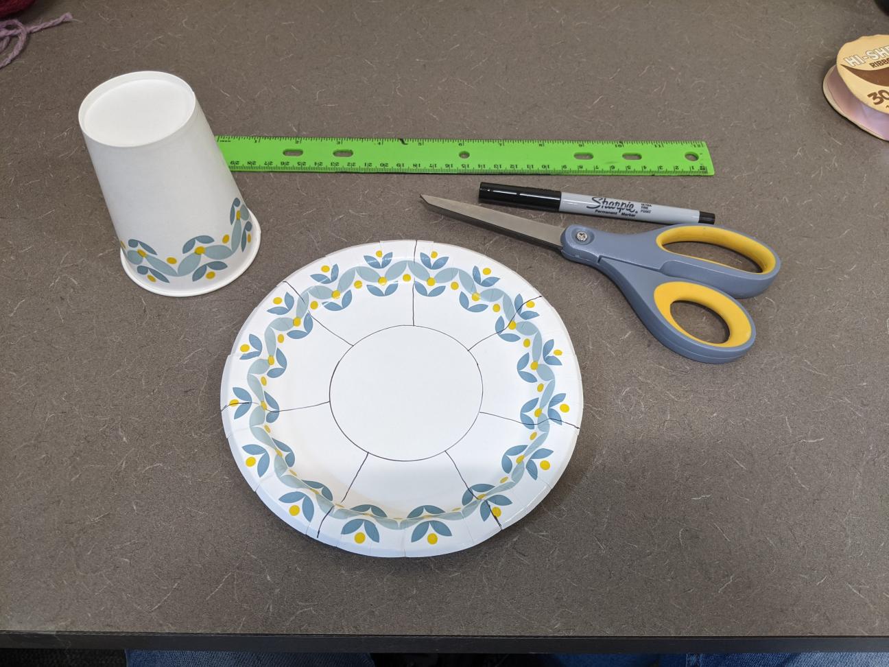 Draw on your paper plate A paper plate and paper cup. The paper plate has a circle and lines drawn on it.