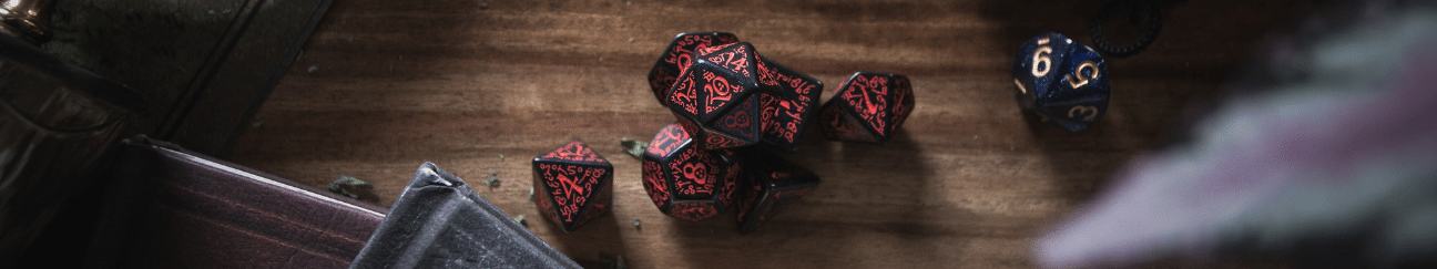 A long, thin banner of a dark wooden tabletop. There is a blurred feather in the foreground. The focal point of the image is a set of black D&amp;D dice with elaborate red accents. Surrounding the dice are several leatherbound books. 