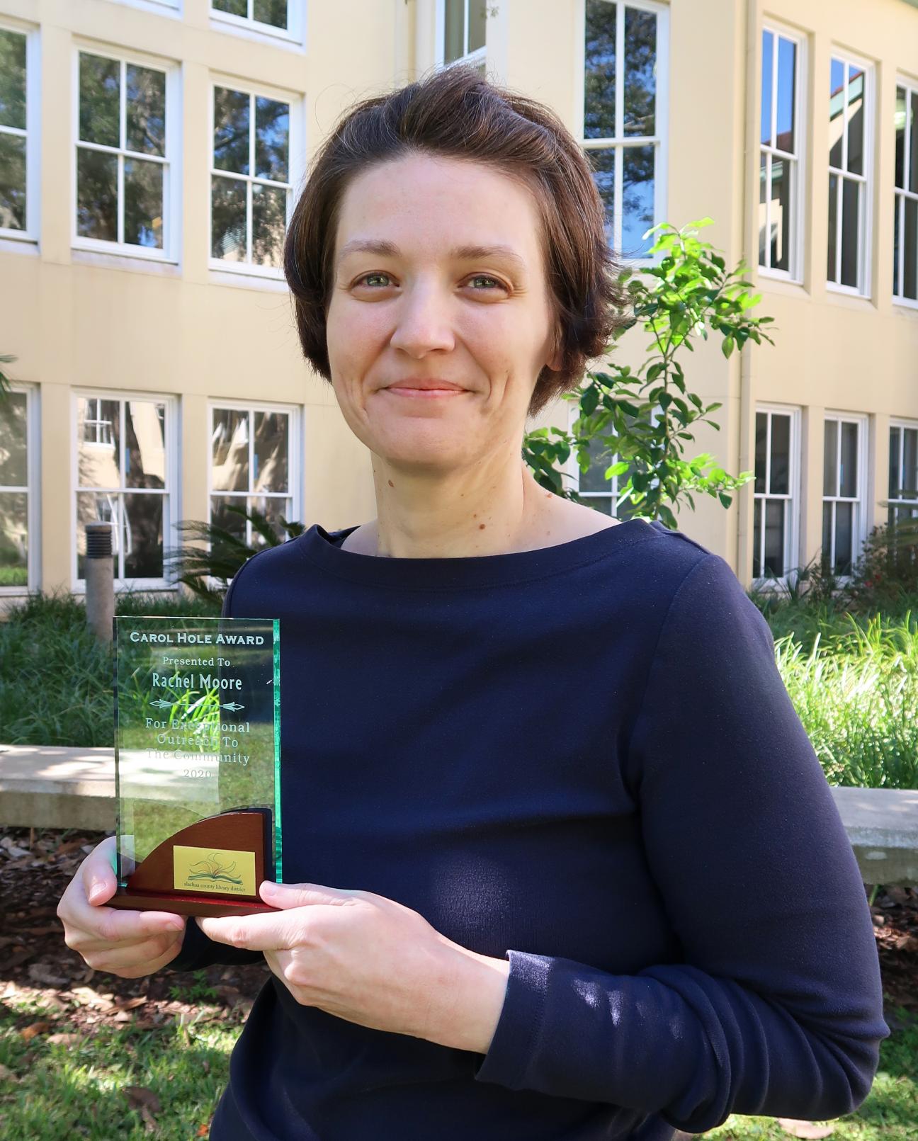 Librarian Rachel Moore holding a glass trophy for the Carol Hole Award.