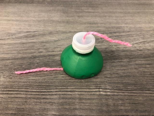 An image of a piece of yarn threaded through the top half of a painted plastic water bottle