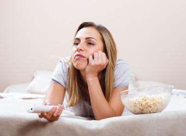 Woman holding a remote with hand on chin looking bored