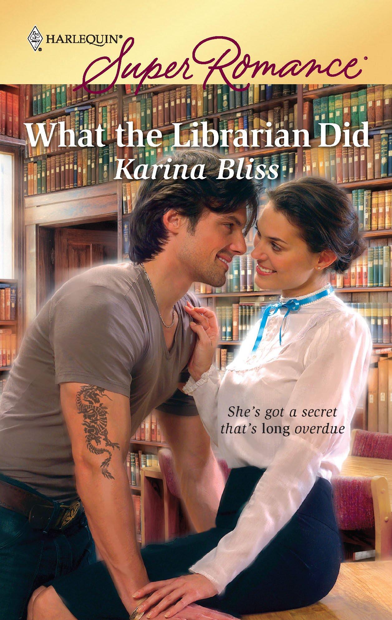 The cover of "What the Librarian Did" by Karina Bliss, which has a brunette woman in a stereotypical "old librarian" outfit sitting on a desk and smiling at a brunette man with a tattoo on his arm who is leaning in for a kiss. 