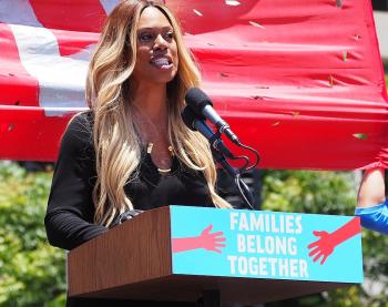 Laverne Cox speaking at a podium at L.A.'s Families Belong Together March in June 2018