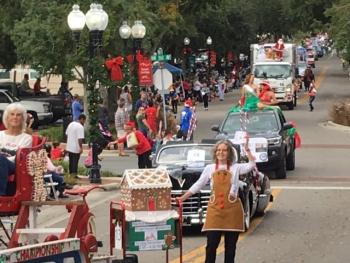 A parade of cars with green and red Christmas decorations drives down Main Street in Alachua