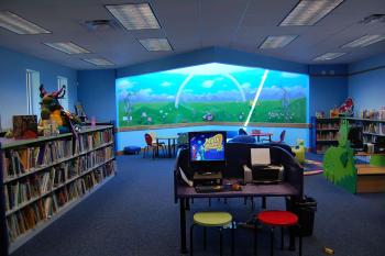 An image of the children's area at Alachua with lots of bright colored books, tables, and a mural of a rainbow.
