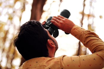A photo of a person holding binoculars, looking up toward the sky. 