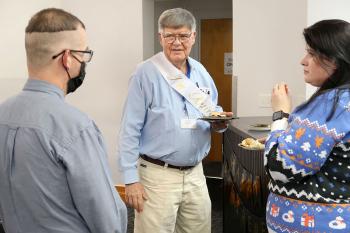 Retiring library specailist Sid Jones stands in the middle of two other people as he talks to them during his retirement party.