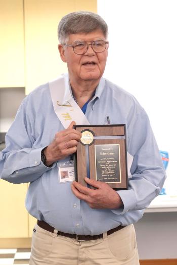 Retiring library specialist Sid Jones poses for a photo while holding his plaque honoring his 36 years of service to the Library District.