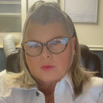White lady with blond hair and glasses looking at the camera in an office