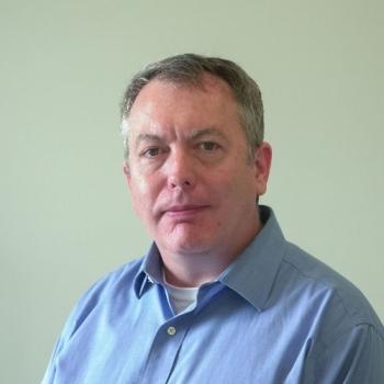 White man with blue dress shirt in front of white background.