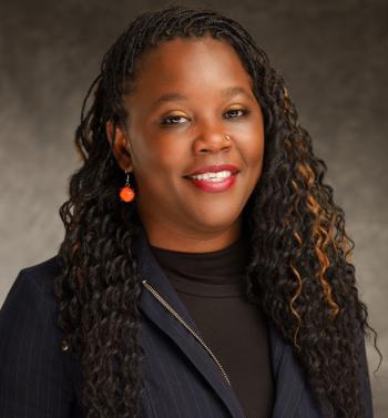 Portrait of local author Maria Green wearing a black suit and orange earrings 