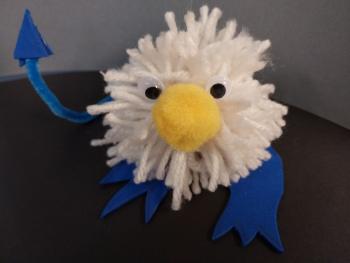 Image of a large white pom pom with googly eyes, small yellow pom pom nose, and felt feet & devil tail.