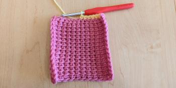 A photo of a pink crochet swatch with the beginning of a yellow border around its edges.