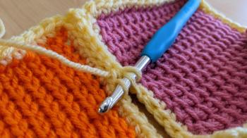 A photo of the orange and pink swatches. There is a crochet hook inserted into the inside loops of the single crochet stitches, in order to stitch the two swatches together