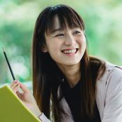 A person smiling while holding a pen and green notebook