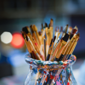 small paint brushes in paint covered glass vase